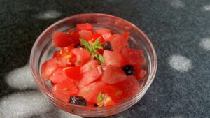 Wassermelonen Salat mit Tomate und Oliven in einer Schüssel, roh und sommerlich angerichtet