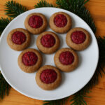 Mulden-Kekse mit Himbeer-Marmelade auf Teller mit Tannenzweigen